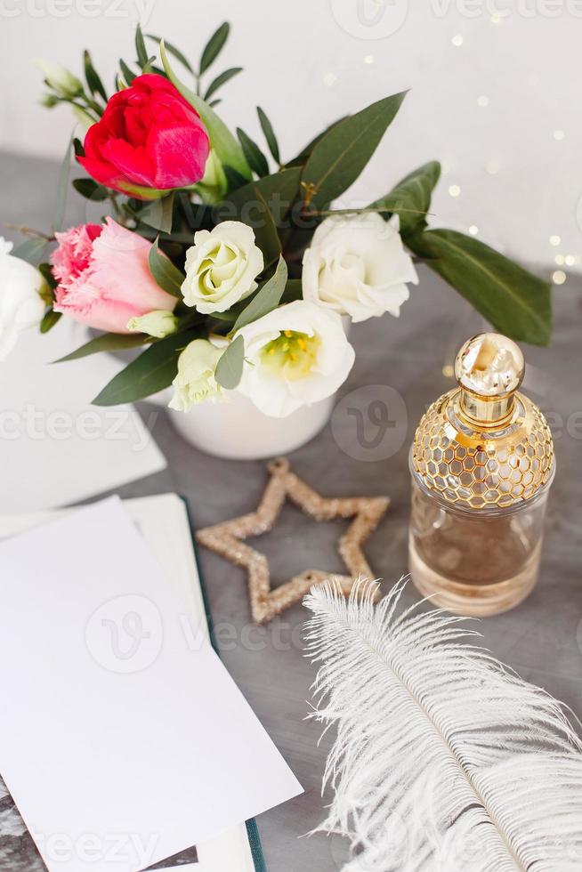 botella de perfume. ramo de primavera sobre mesa de hormigón gris. rosas, tulipanes y lisianthus. pluma blanca. foto