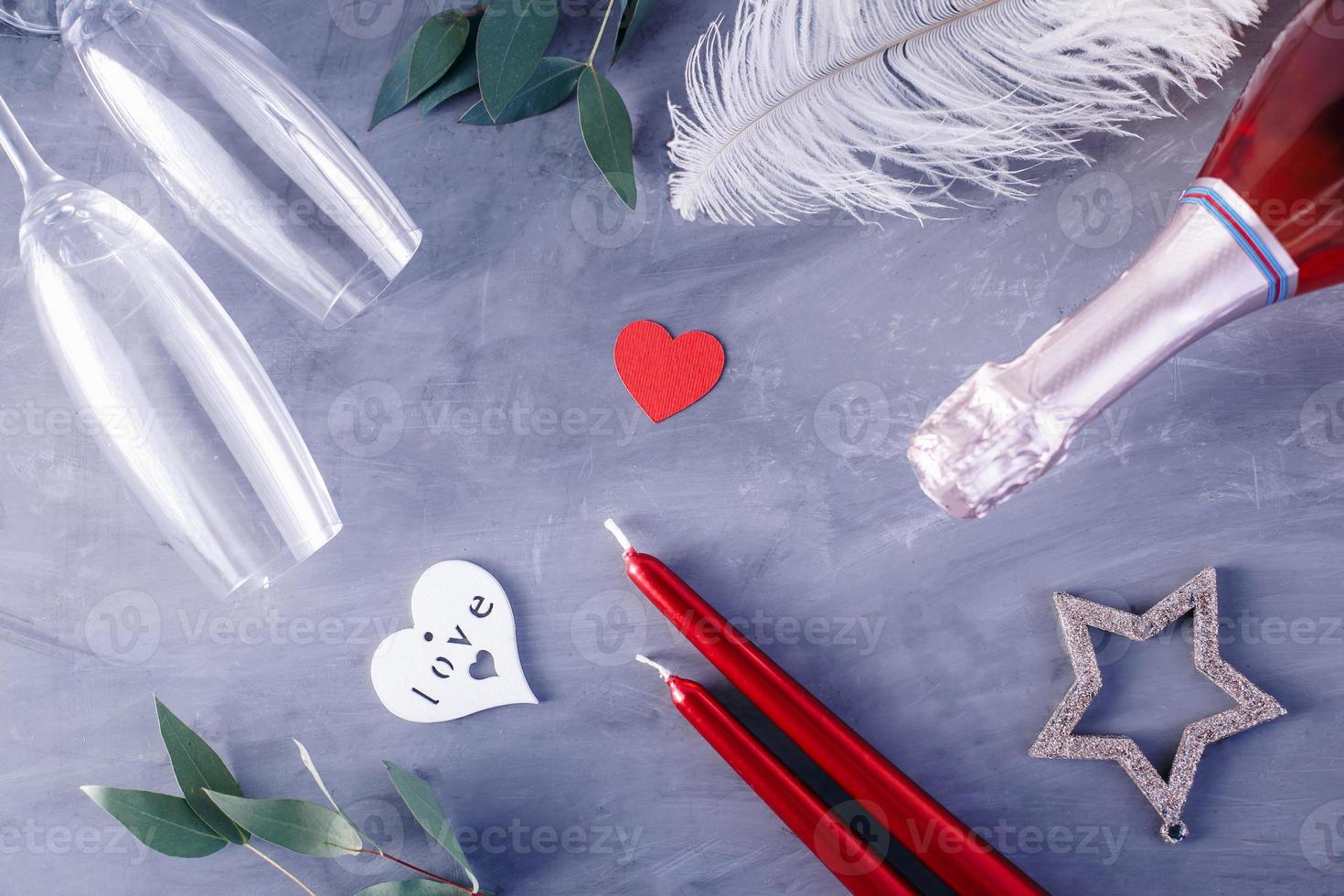 Flat lay composition with bottle of champagne, candles, feather and hearts for celebration on grey concrete background. Glass for champagne. photo