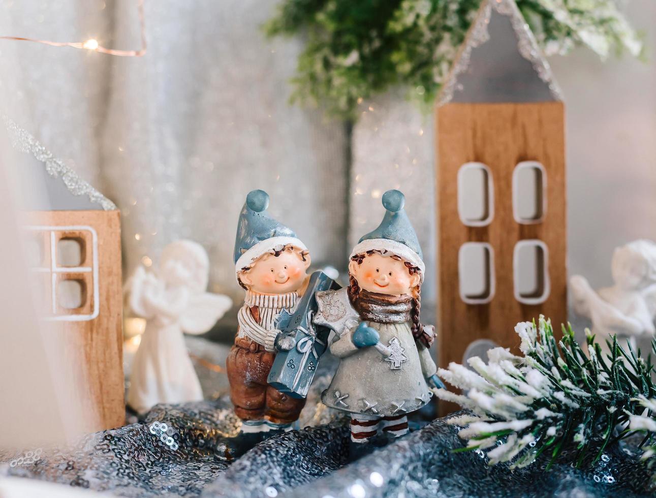 Porcelain figurines of children in a Christmas decor. Winter figurines of a boy and a girl with gifts on the background of houses and cones. Christmas Greeting Card. Copy space. photo