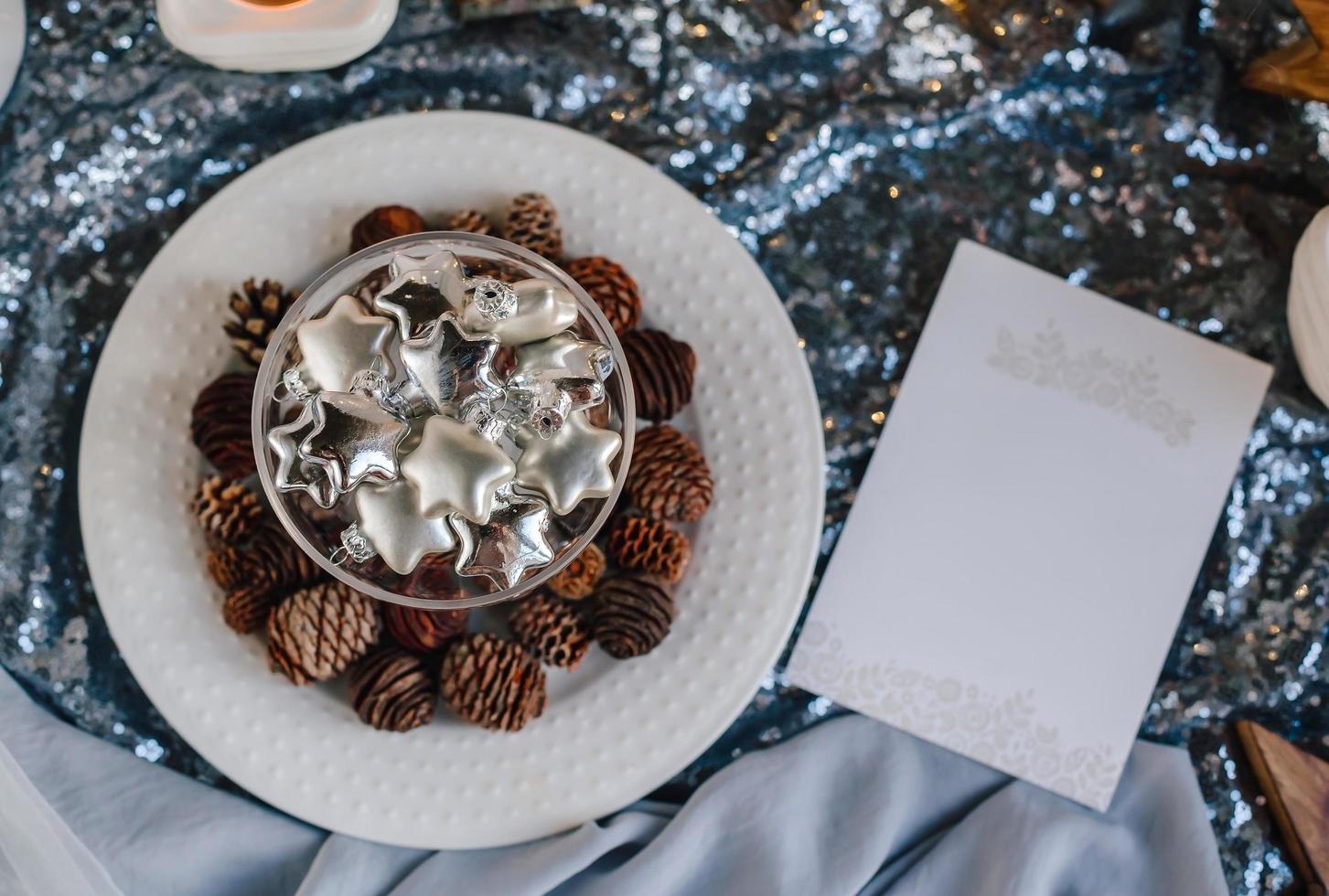 Glass silver stars in a glass vase. Christmas tree toys in a glass on a background of shiny fabric and fir cones. Copy space. photo