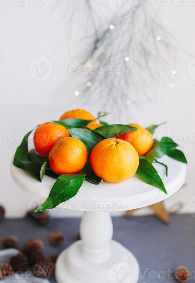 mandarinas naranjas sobre fondo gris en la decoración de año nuevo con piñas marrones y hojas verdes. decoración navideña con mandarinas. deliciosa dulce clementina. foto