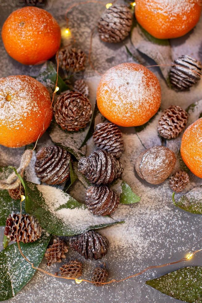 Orange tangerines on grey background in New Year's decor with brown pine cones and green leaves. Christmas decoration with mandarins. Delicious sweet clementine. photo