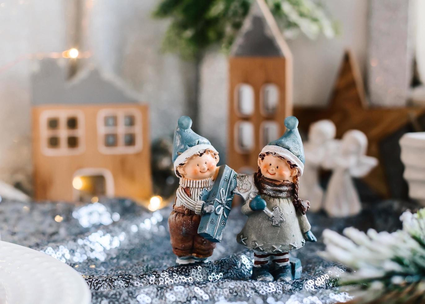 figuritas de porcelana de niños en una decoración navideña. figuras de invierno de un niño y una niña con regalos en el fondo de casas y conos. tarjeta de felicitación de navidad. copie el espacio foto