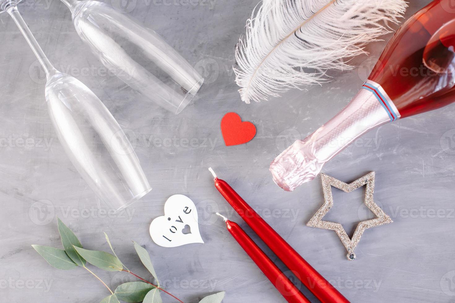 Flat lay composition with bottle of champagne, candles, feather and hearts for celebration on grey concrete background. Glass for champagne. photo