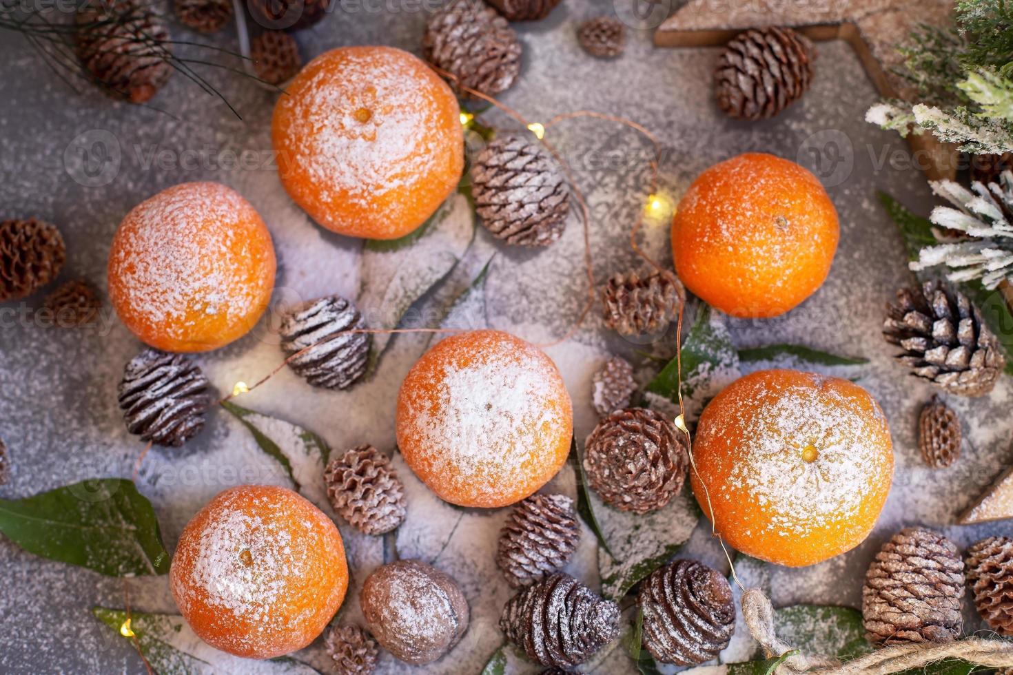 Orange tangerines on grey background in New Year's decor with brown pine cones and green leaves. Christmas decoration with mandarins. Delicious sweet clementine. photo