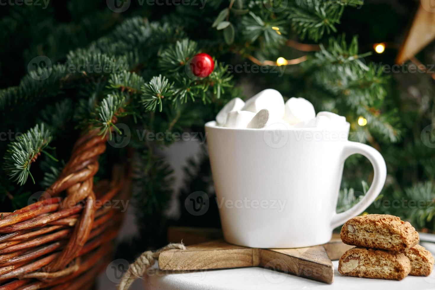 Coffee in a white cup with marshmallows. Morning festive coffee with traditional Italian cantuccini almond cookies. A cup of coffee on a background of green fir branches on a white stand. photo