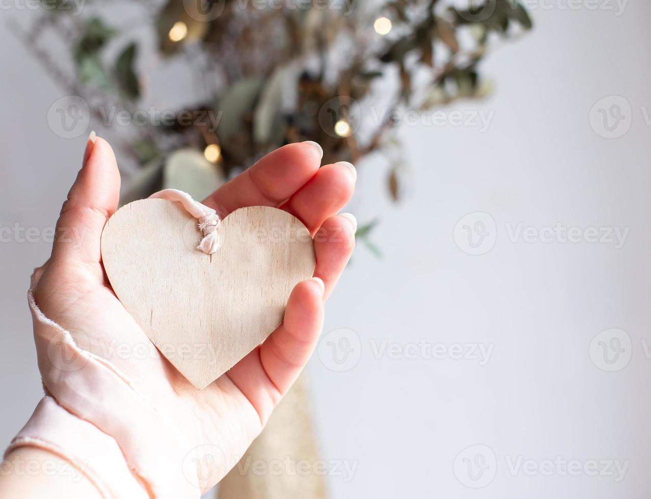 Light wooden heart on a silk pink ribbon on white background. Space for text. Hand holding a wooden heart pendant on a chiffon pale pink ribbon. Copy space. photo