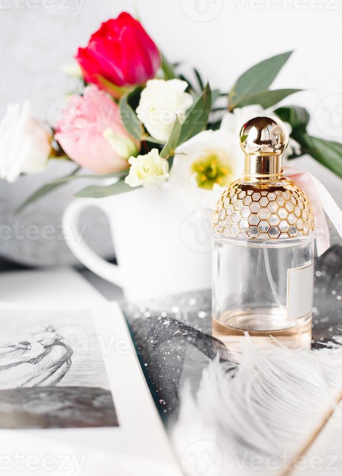 Bottle of perfume. Spring bouquet on gray concrete table. Roses, tulips and lisianthus. White feather. photo