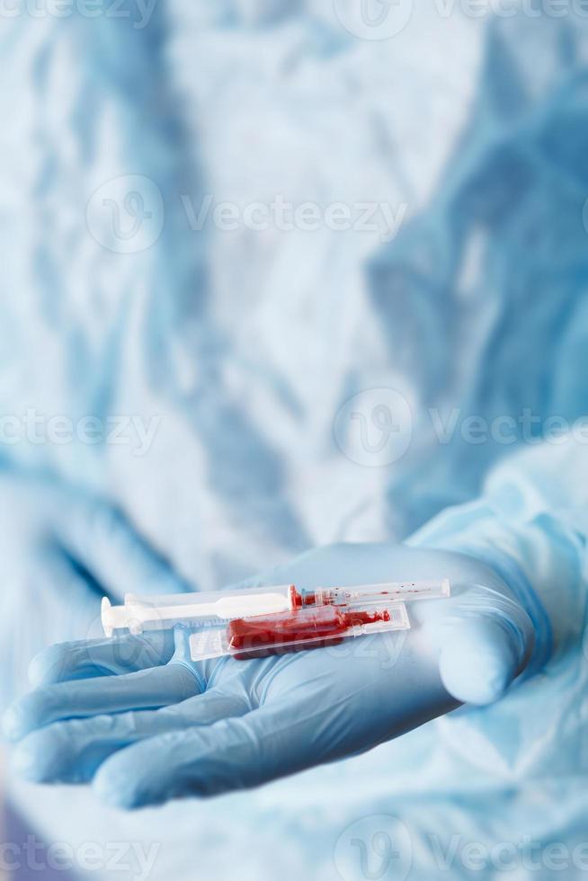 Close up of doctor hand holding syringe and blood sample. Medical equipment. Blood test. A doctor wearing personal protective equipment including mask, goggle, and suit to protect COVID-19 photo