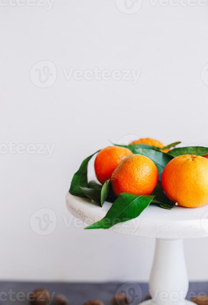 mandarinas naranjas sobre fondo gris en la decoración de año nuevo con piñas marrones y hojas verdes. decoración navideña con mandarinas. deliciosa dulce clementina. foto