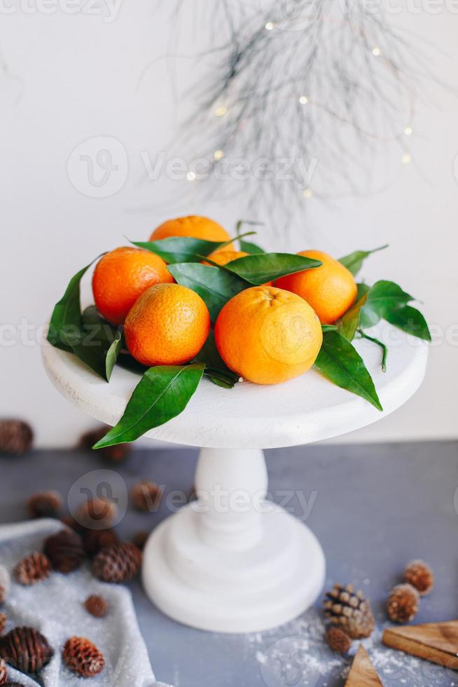 mandarinas naranjas sobre fondo gris en la decoración de año nuevo con piñas marrones y hojas verdes. decoración navideña con mandarinas. deliciosa dulce clementina. foto