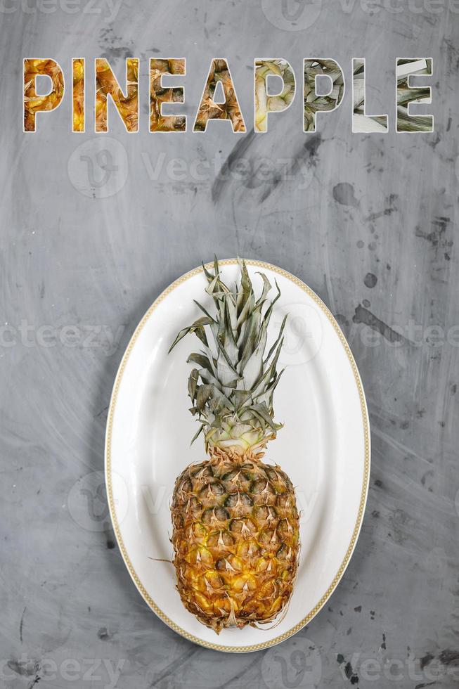 White Plate with Ripe Whole Pineapple on Grey Concrete Background. Word Pineapple. photo