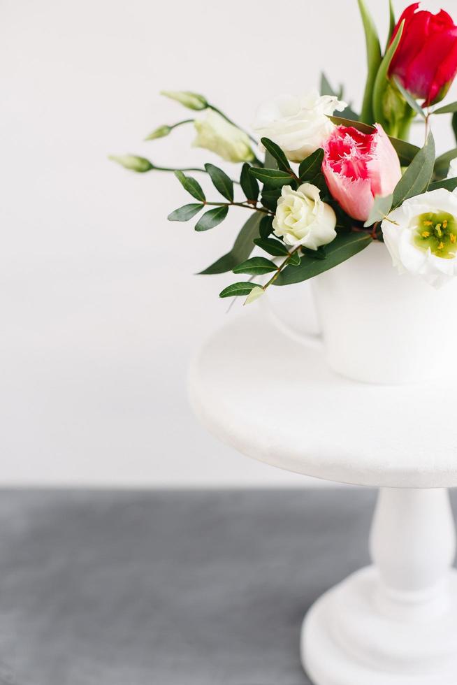 ramo de primavera en jarrón blanco sobre soporte blanco de madera. rosas, tulipanes y lisianthus. foto