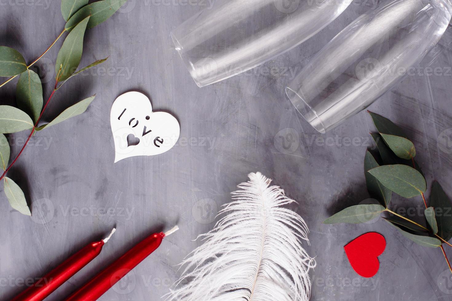 Flat lay composition with bottle of champagne, candles, feather and hearts for celebration on grey concrete background. Glass for champagne. photo