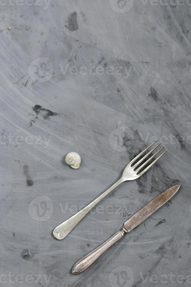 caracol, tenedor y cuchillo sobre fondo de hormigón gris. copie el espacio foto