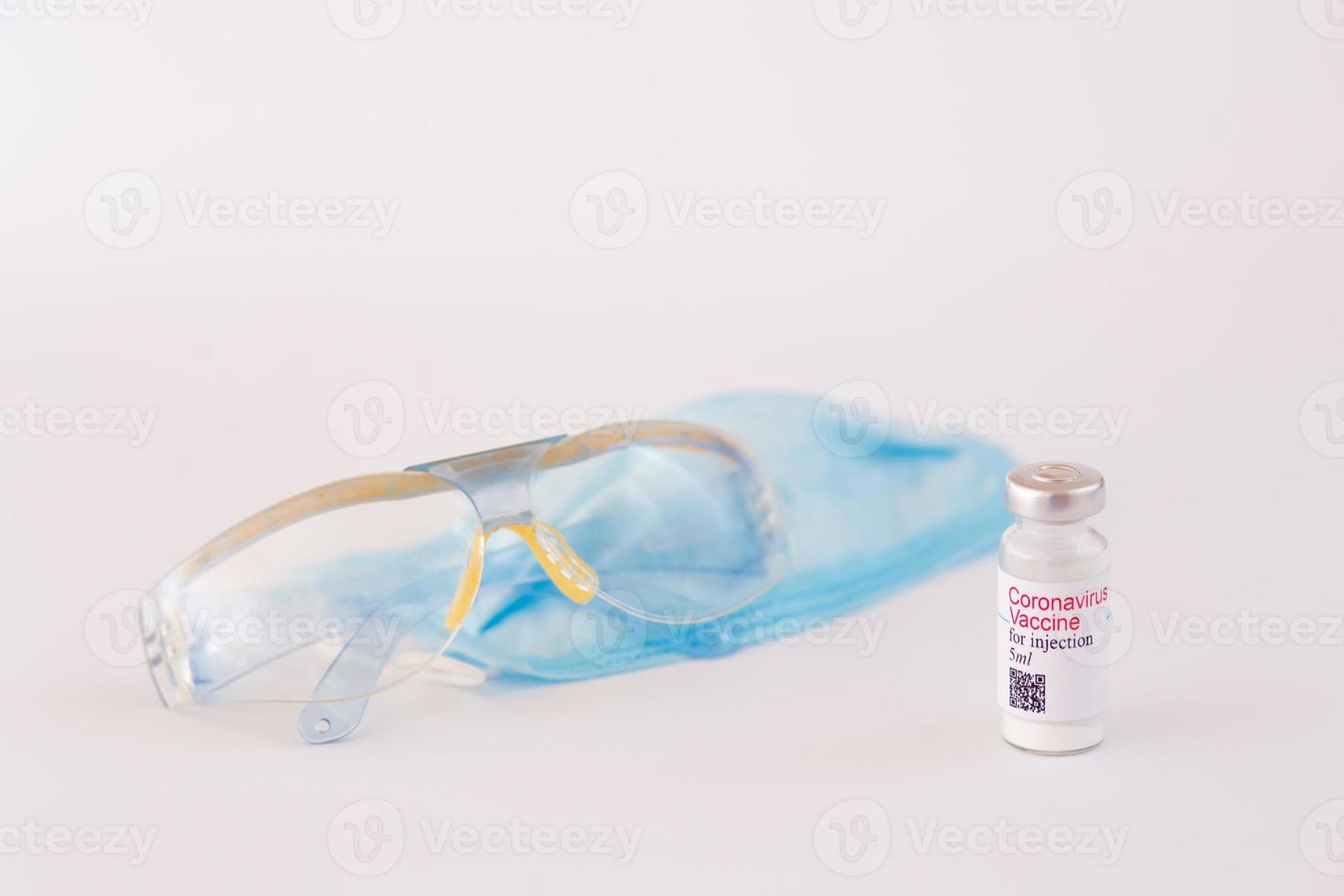 Coronavirus vaccine. Medical preparation in ampoule. Treatment for the disease, covid-19. The vaccine on a white background and on the background of a syringe, rubber gloves and goggles photo