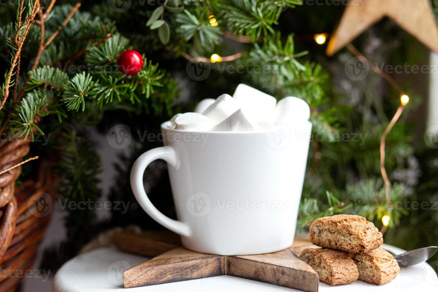 Coffee in a white cup with marshmallows. Morning festive coffee with traditional Italian cantuccini almond cookies. A cup of coffee on a background of green fir branches on a white stand. photo