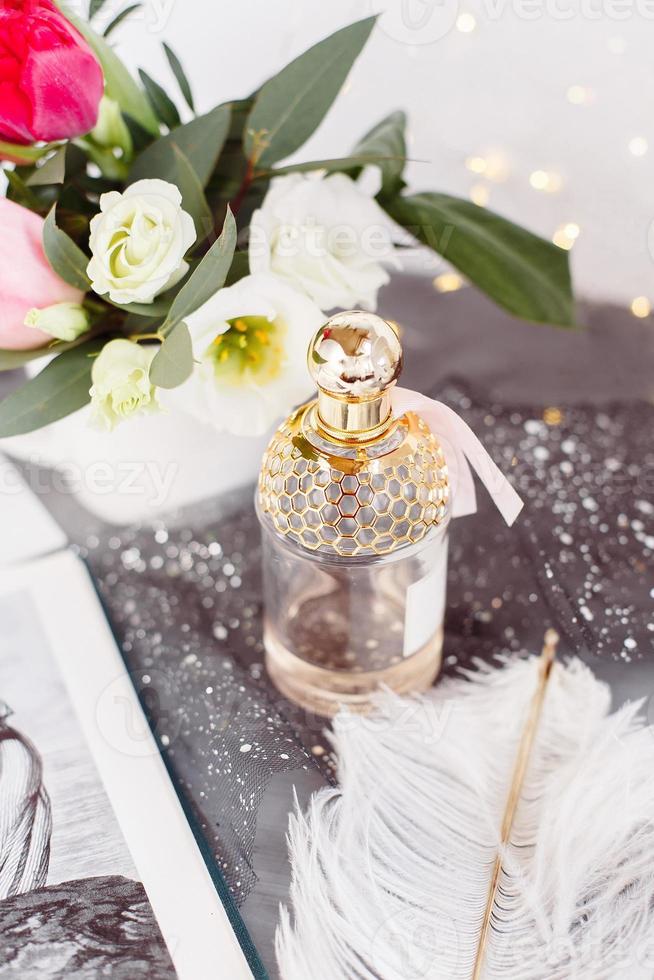 Bottle of perfume. Spring bouquet on gray concrete table. Roses, tulips and lisianthus. White feather. photo