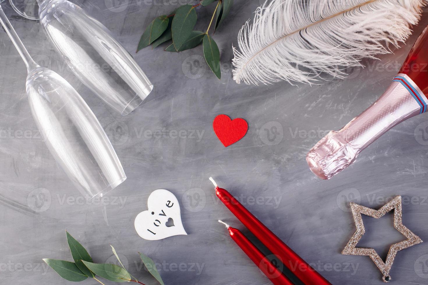Flat lay composition with bottle of champagne, candles, feather and hearts for celebration on grey concrete background. Glass for champagne. photo