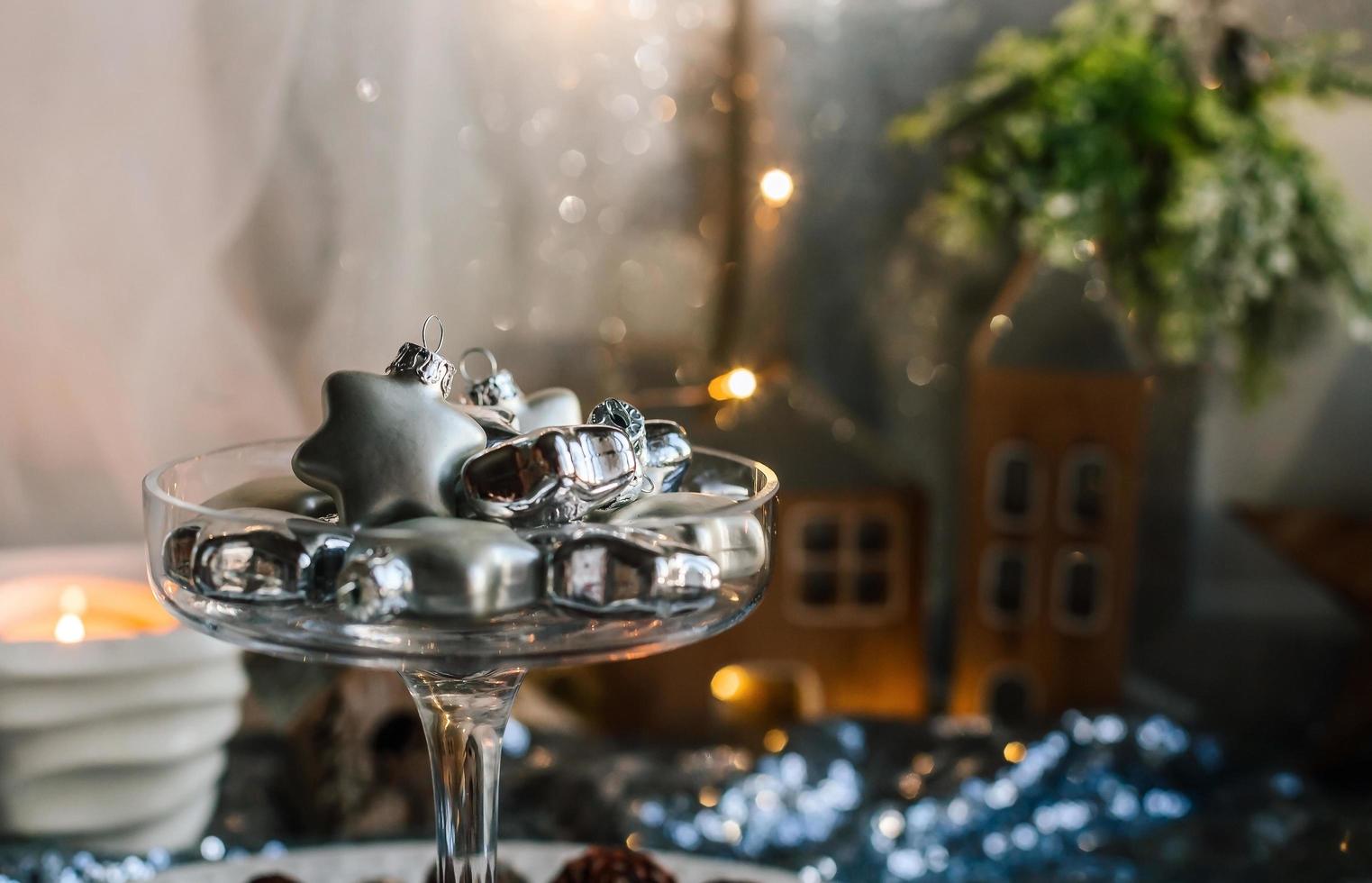 Glass silver stars in a glass vase. Christmas tree toys in a glass on a background of shiny fabric and fir cones. Copy space. photo