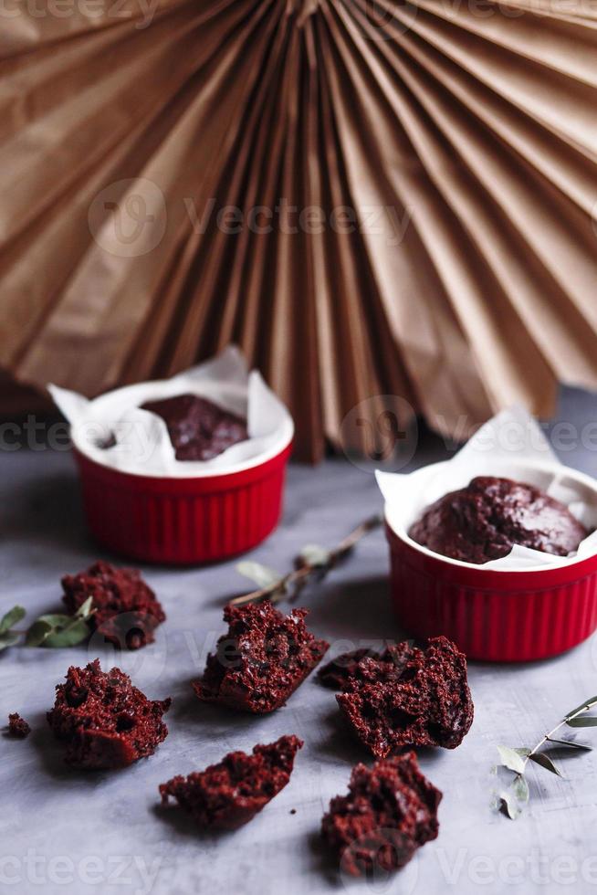 muffins de chocolate en tazas rojas. pequeño ramekin de cerámica vidriada con pasteles marrones sobre un fondo gris y blanco. foto
