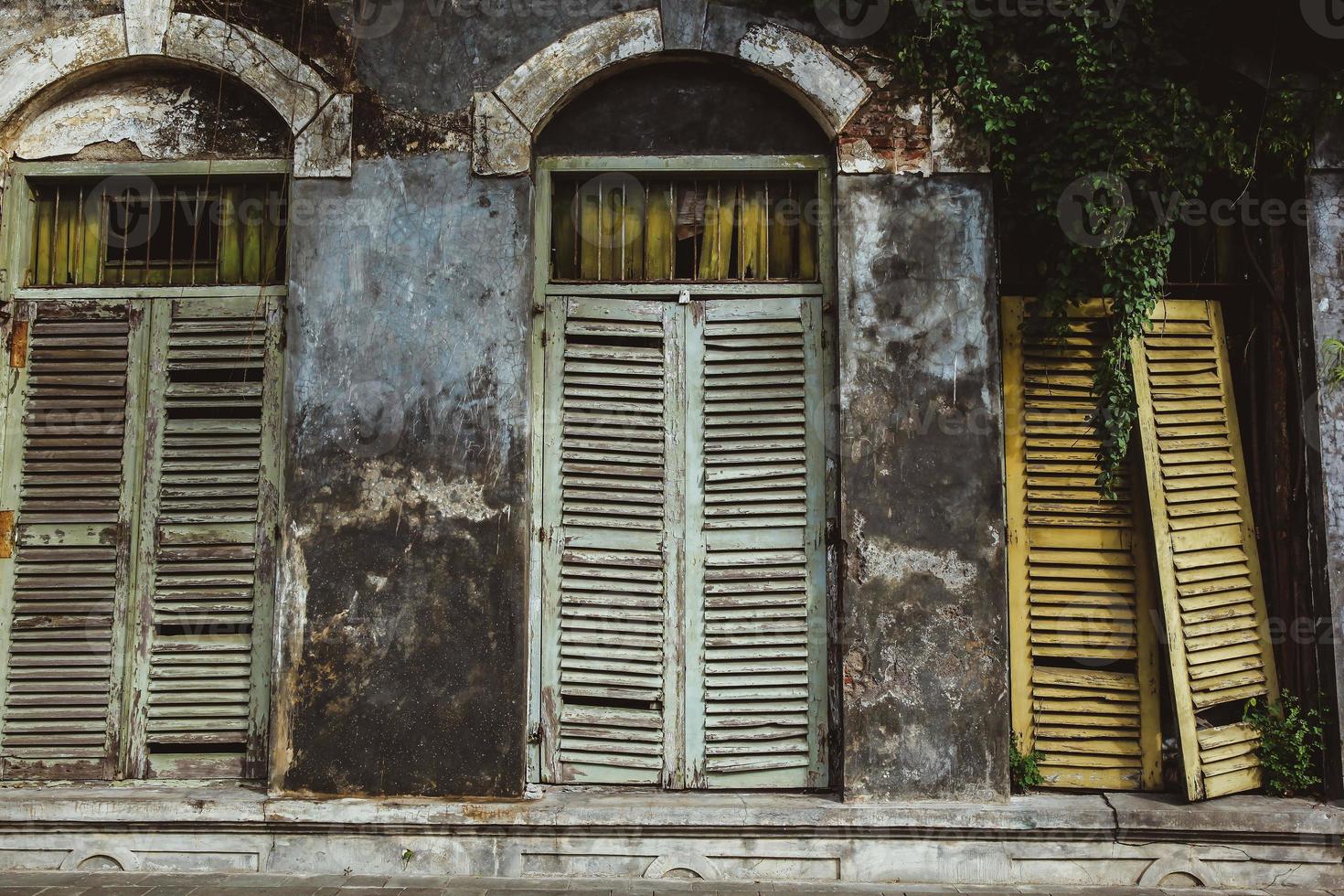 Facade of an old abandoned building with mossy wall and broken wooden windows photo