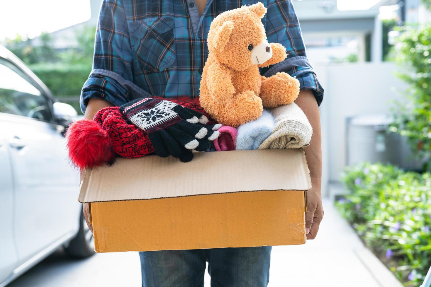 Holding clothing donation box with used clothes and doll at home to support help for poor people in the world. photo