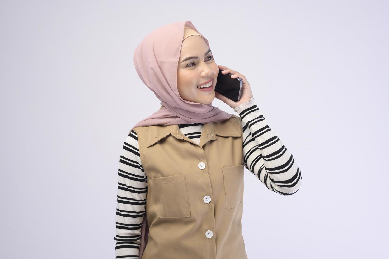 Portrait of beautiful woman with hijab using cellphone on white background photo