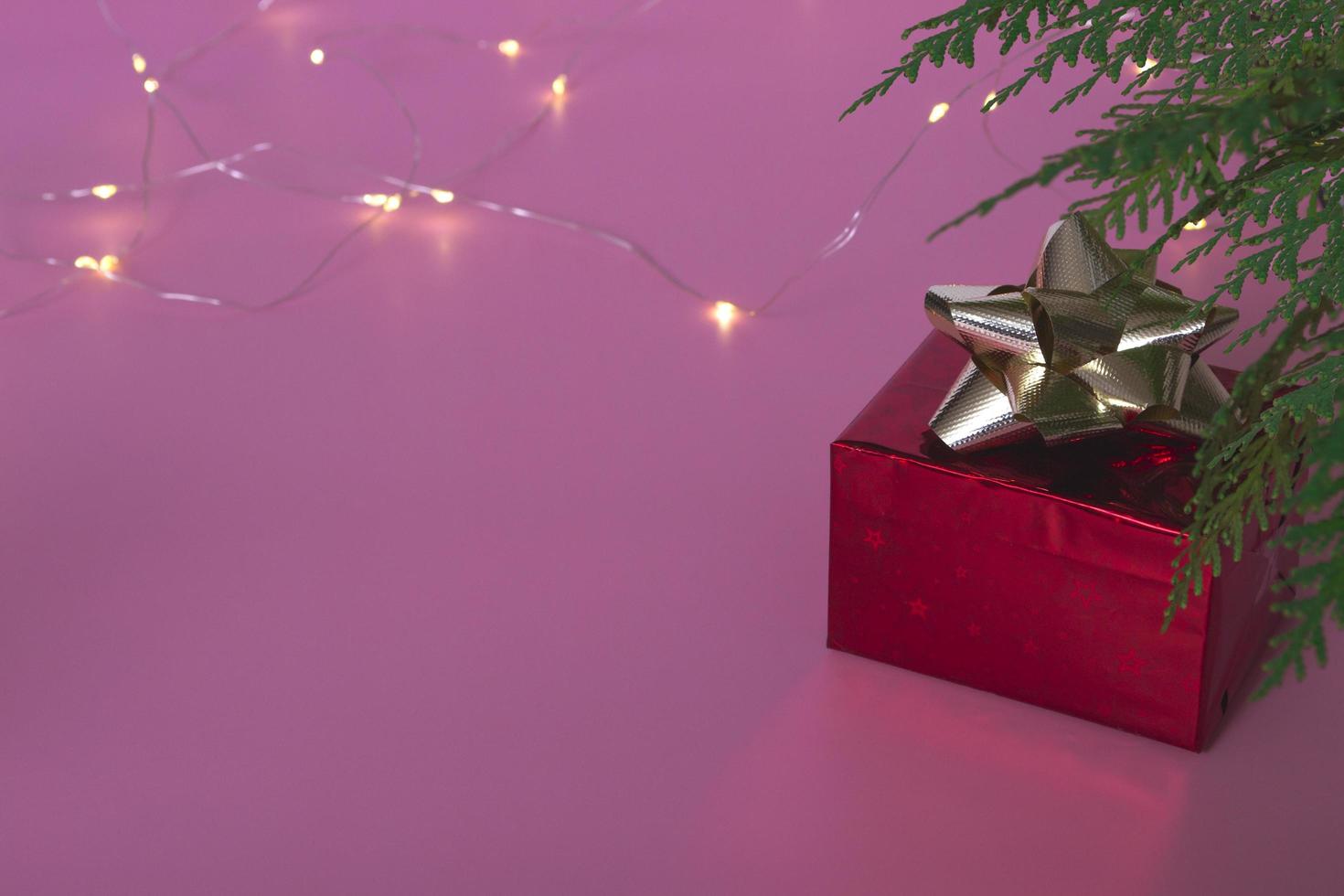 Festive concert.Gift red box under the Christmas tree on a pink background with a garland. Close up copy space. Holiday postcard. photo