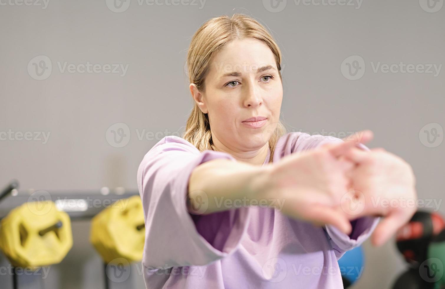 woman stretching her arms in a gym, warming up before training, workout in fitness club, real people. healthy lifestyle. photo