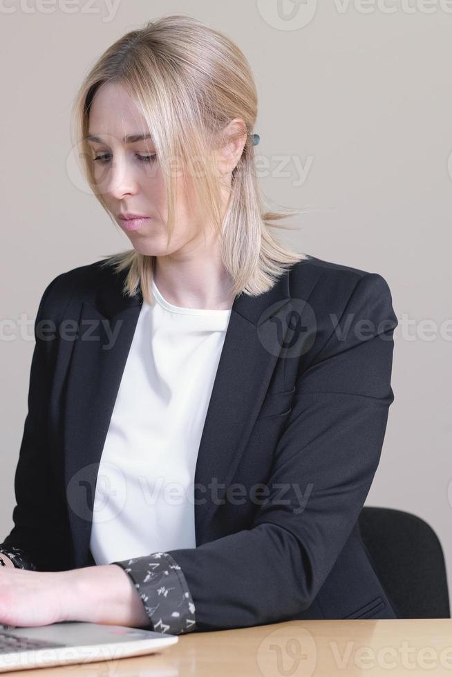 Focused blond businesswoman in formal outfit working on laptop computer, typing on keyboard, or checking email sitting in office, concentrated woman working online photo