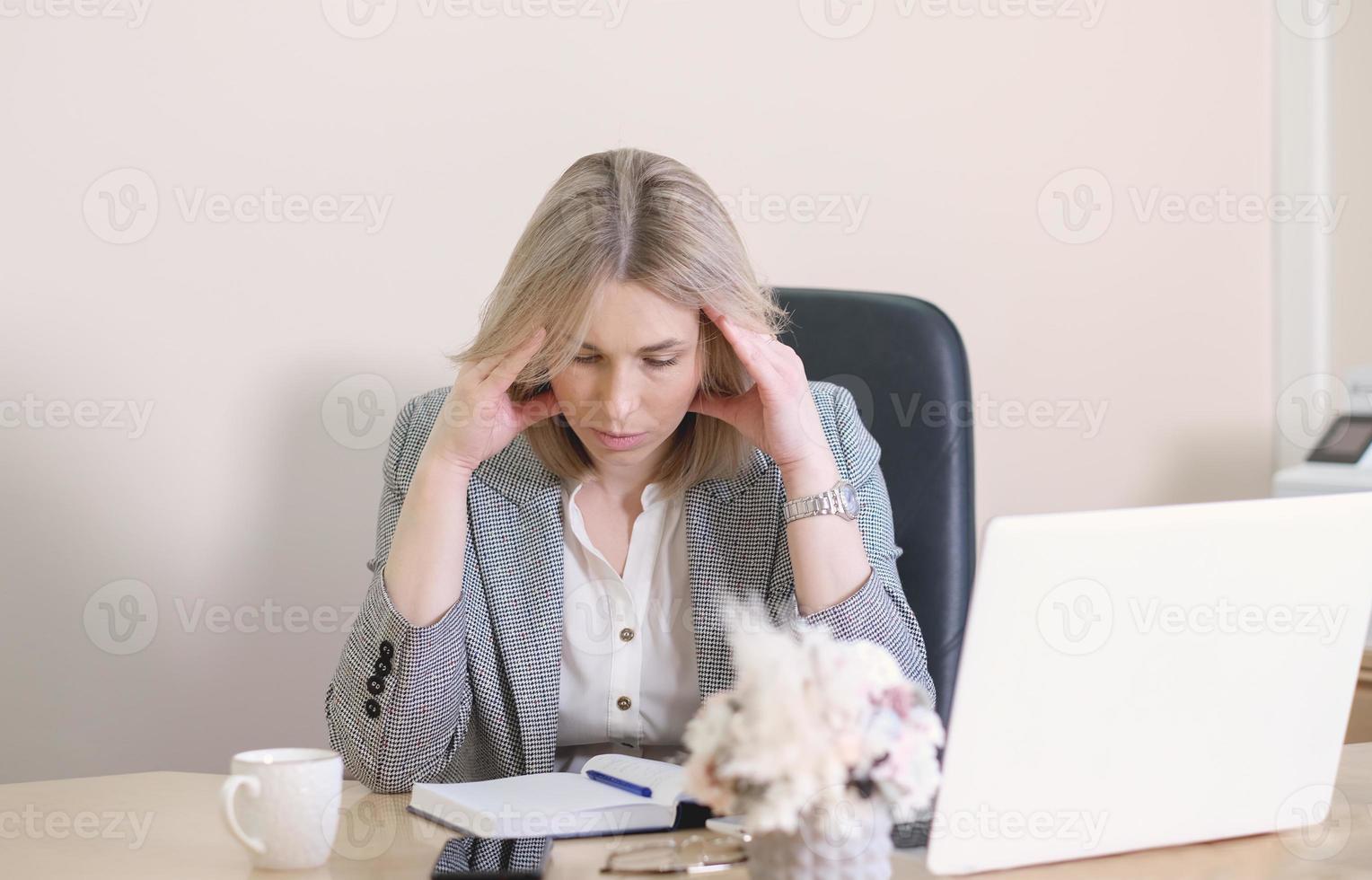 estresada y desconcertada mujer de negocios rubia mirando el diario, sentada en la oficina, exhausta empleada disgustada, teniendo problemas con un difícil proyecto en línea. foto