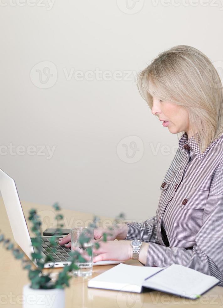 blond business woman working in an office, typing on a laptop. caucasian woman secretary or manager working on computer. side view photo