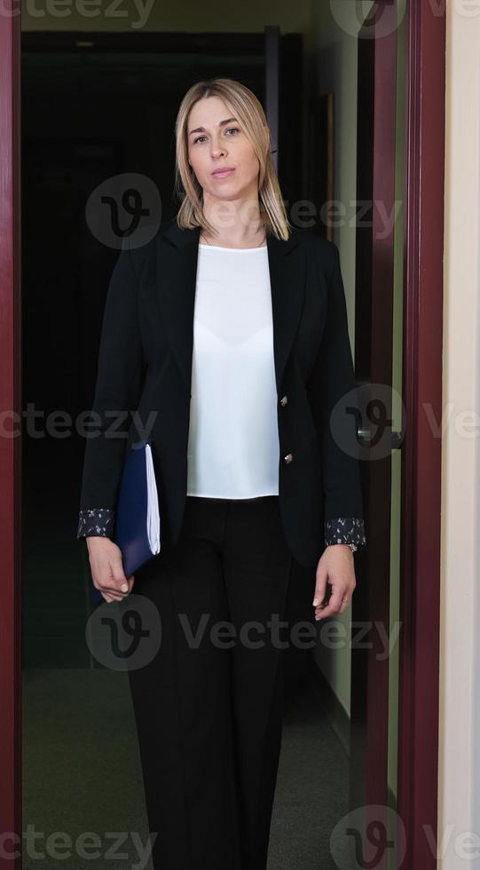 woman legal adviser or lawer wearing formal clothes standing next to door and holding documents. young judge assistant or attorney coming into office photo