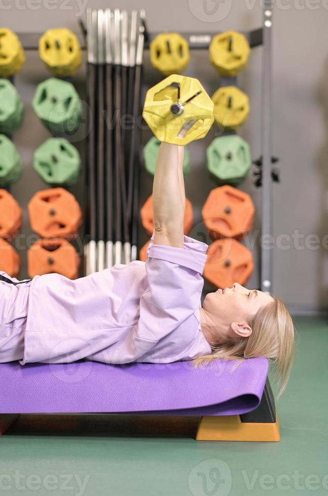 woman lying on training bench lifting barbell in gym, pushing exercise training chest muscles health and fitness concept, vertical. photo