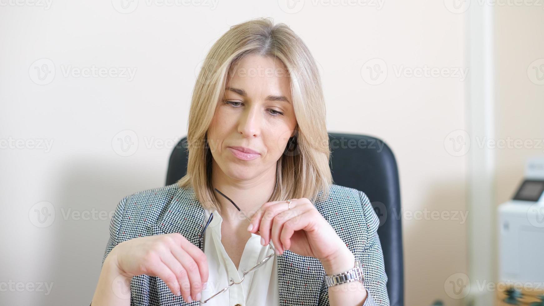 business woman holding glasses and looking downwards. thinking on daily tasks and goals. blond female manager working in office. photo