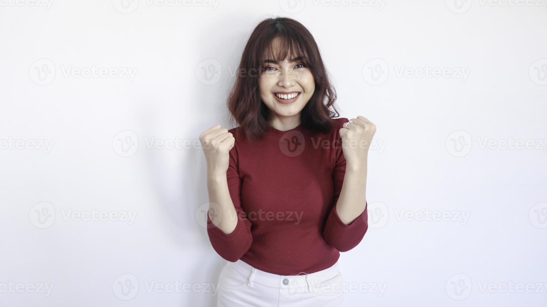 feliz y ganadora hermosa chica asiática con camisa roja en fondo blanco foto