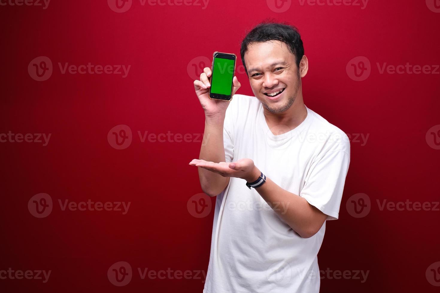 Smile Young Asian man pointing on green blank space on smartphone on red background. photo