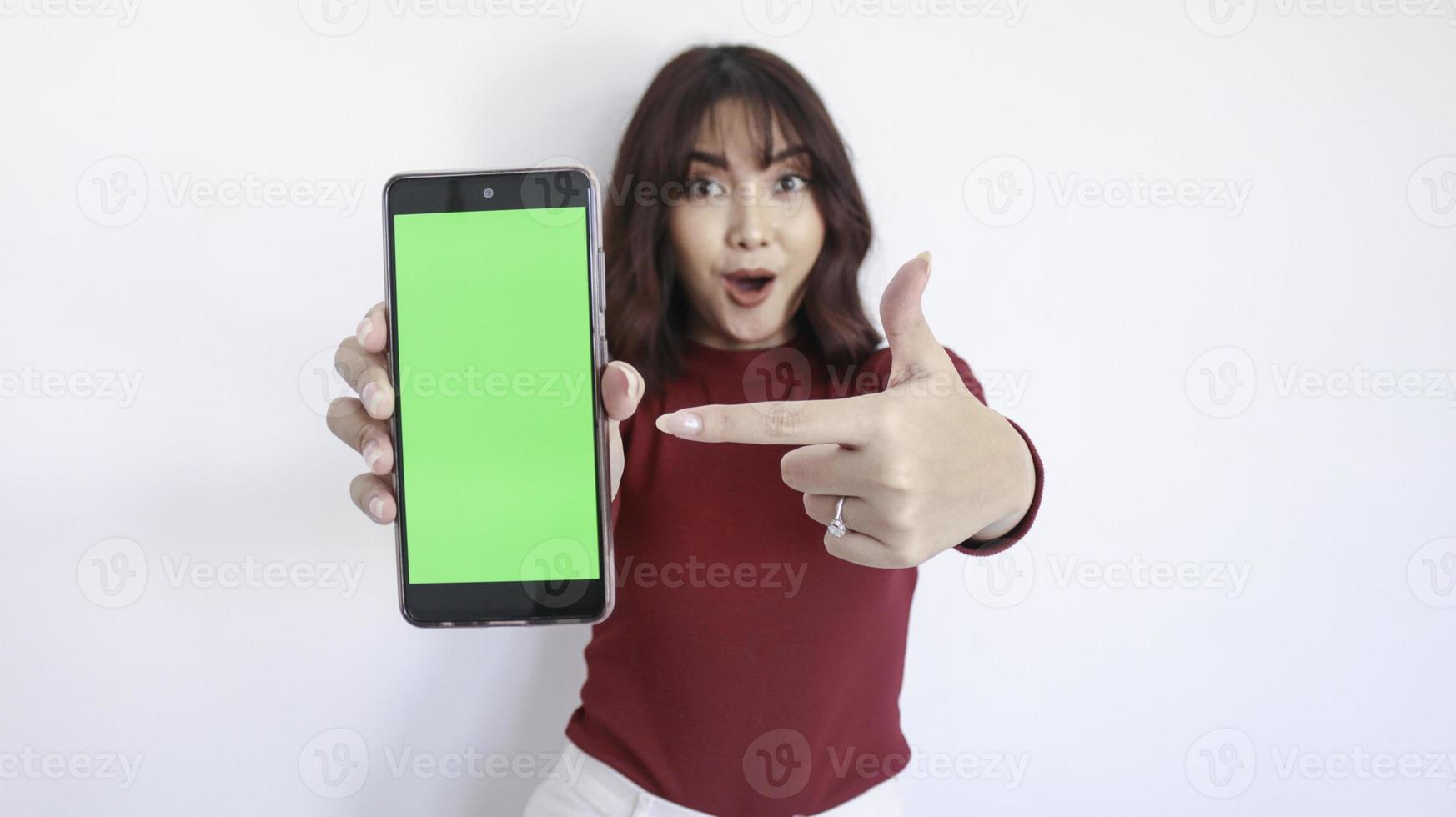 Wow and Shock Asian beautiful girl point on green screen phone with blurry background on face in white photo