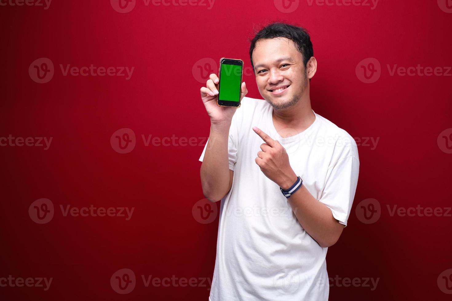 Smile Young Asian man pointing on green blank space on smartphone on red background. photo