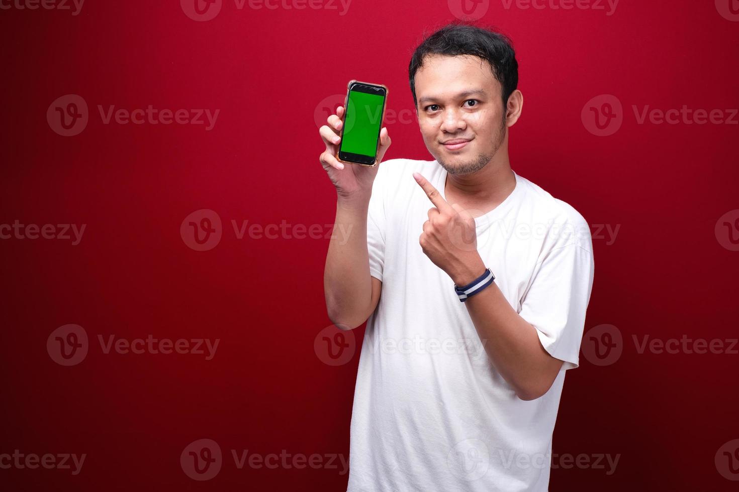 Smile Young Asian man pointing on green blank space on smartphone on red background. photo