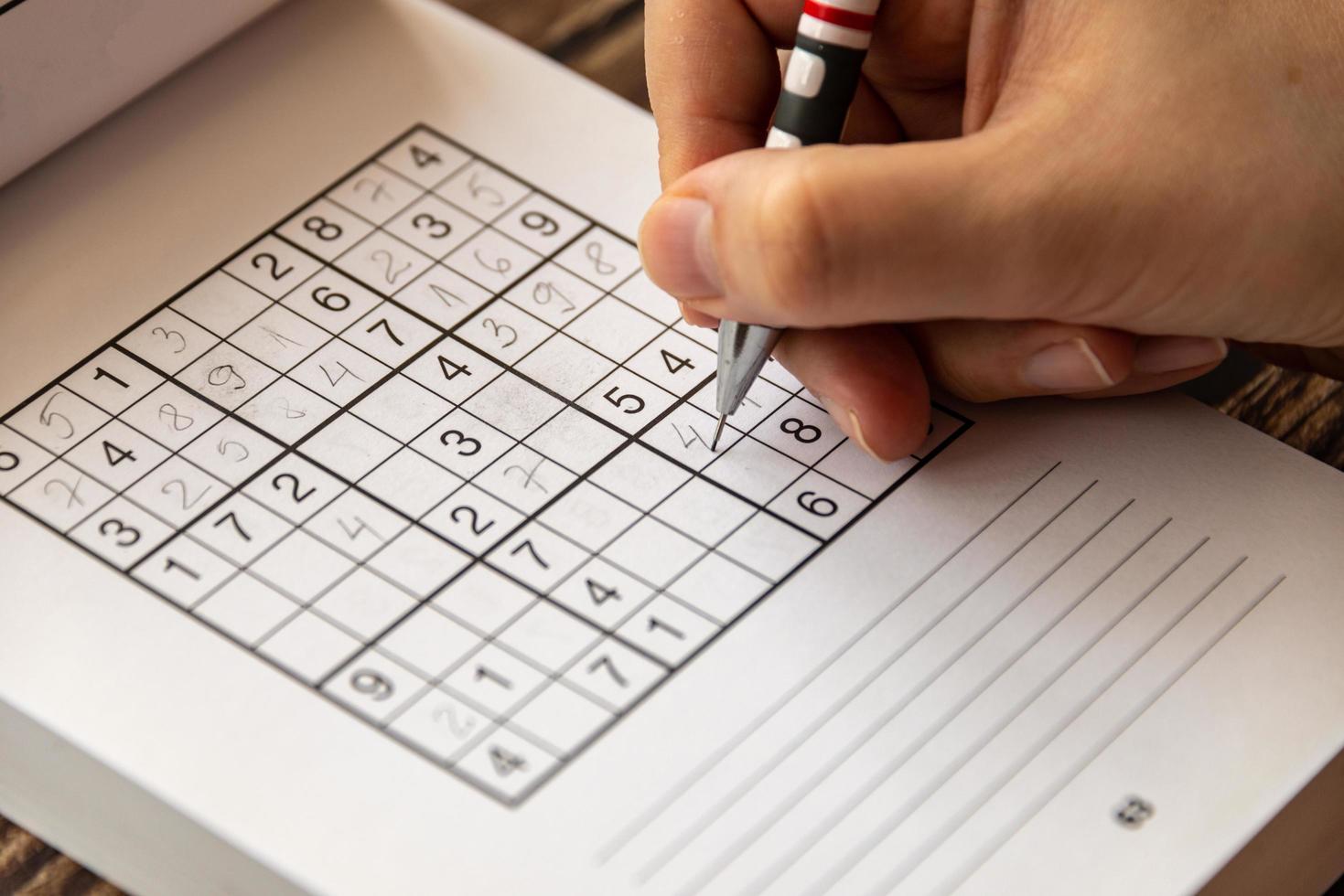 A person solving a sudoku puzzle on a wooden table photo