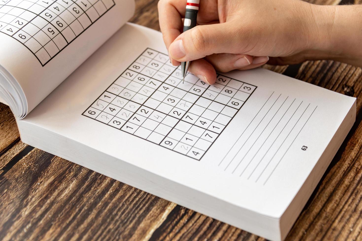 A person solving a sudoku puzzle on a wooden table photo