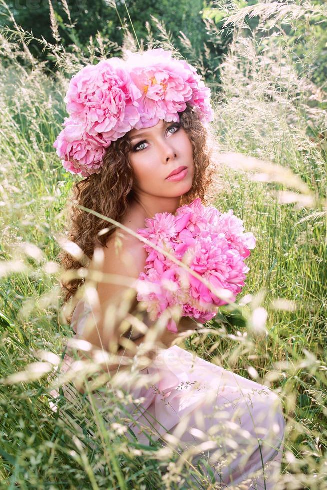 hermosa mujer caucásica con una corona de peonías rosas en la cabeza. primavera, flor, concepto de hadas foto