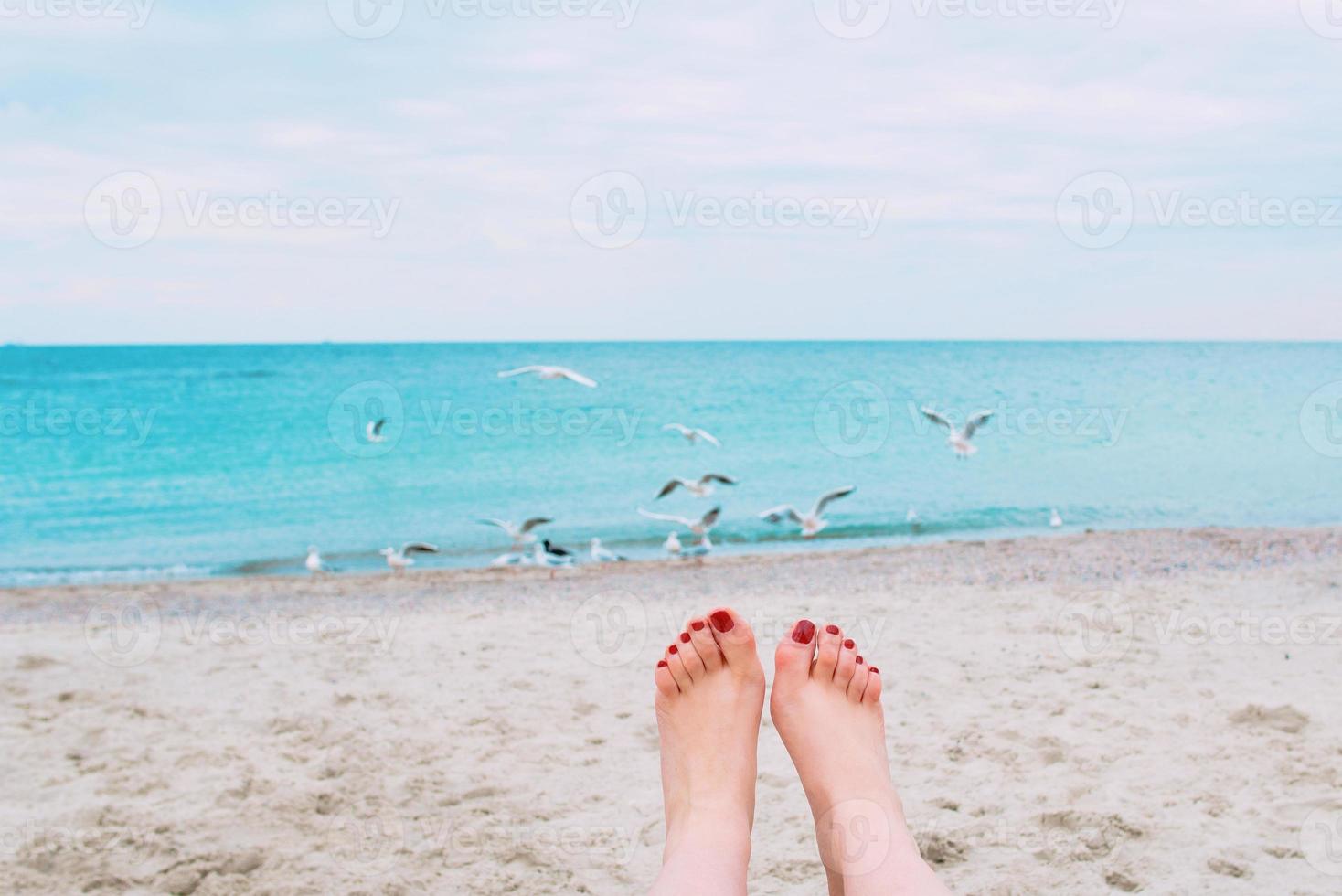 woman's feets with red nails on the sea shore background photo