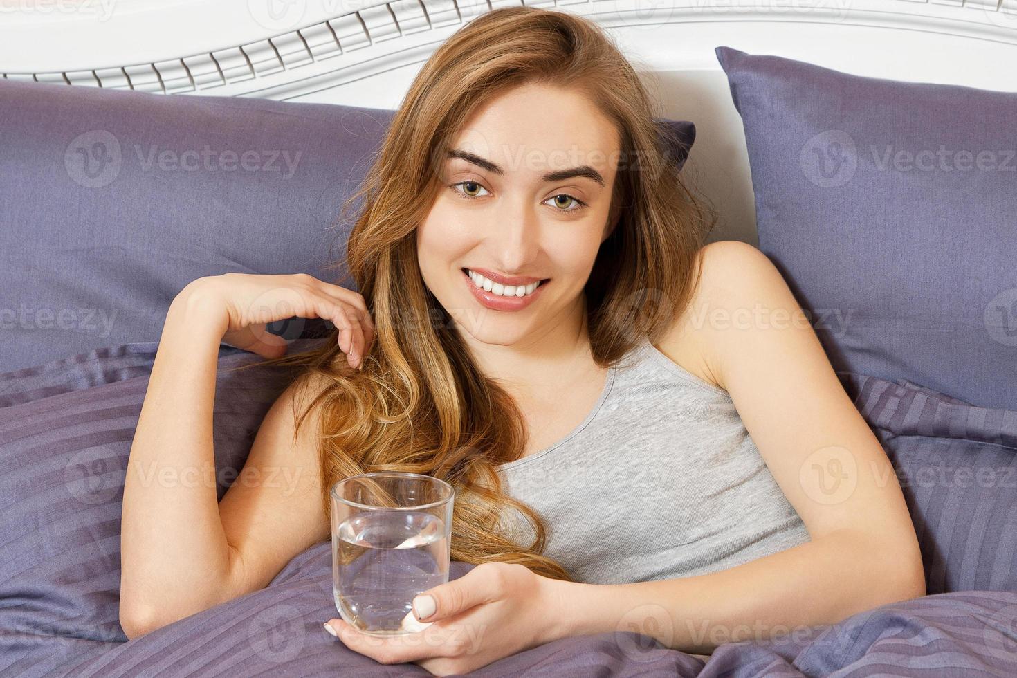 Woman hangover, woman hold glass of water lying on bed. Girl with head pain close up. young woman feel sick in the morning, headache or toxemia of pregnancy photo