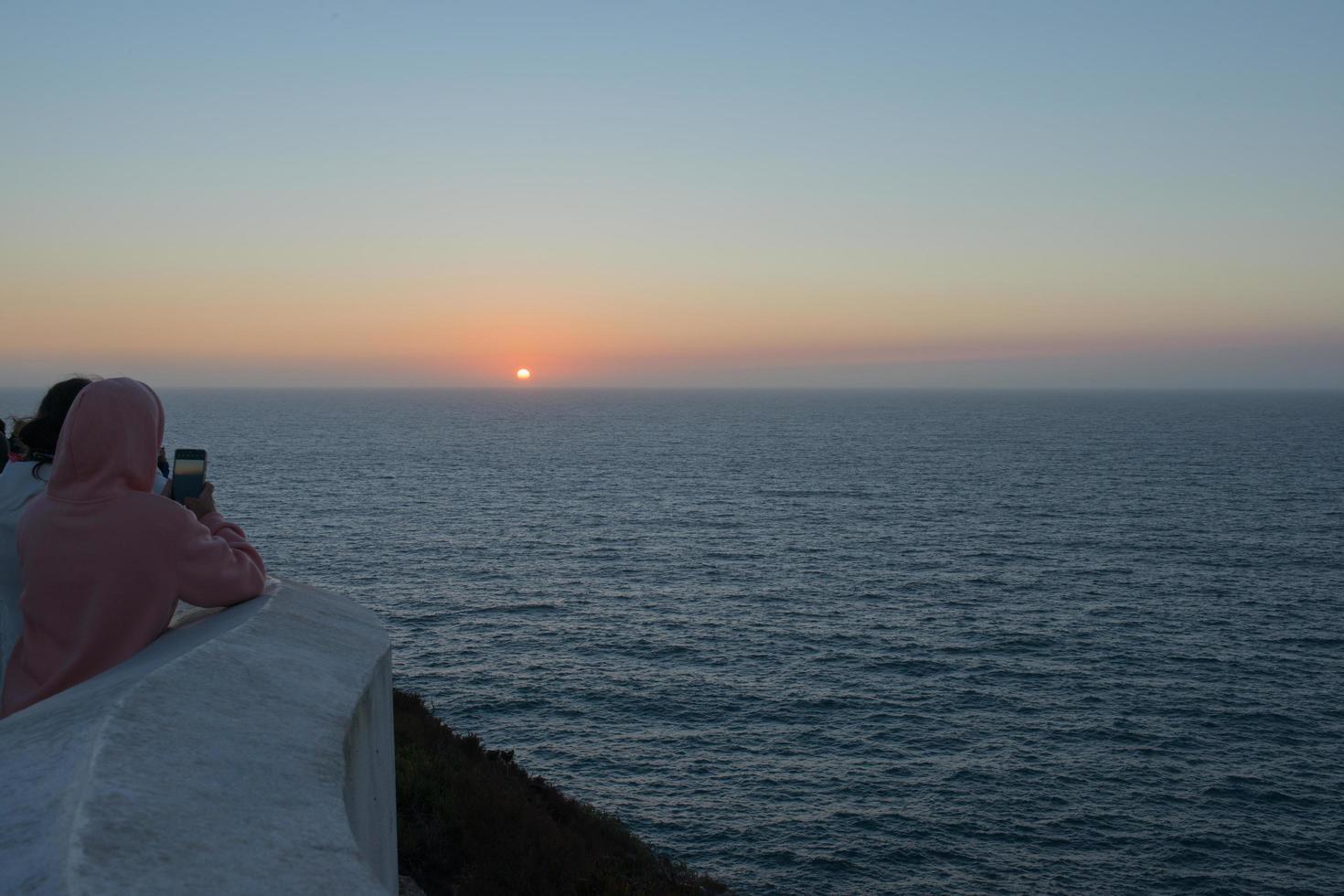 grupo de personas irreconocibles mirando la puesta de sol y tomando fotos con sus móviles. cabo de san vicente, fin de europa. Portugal.