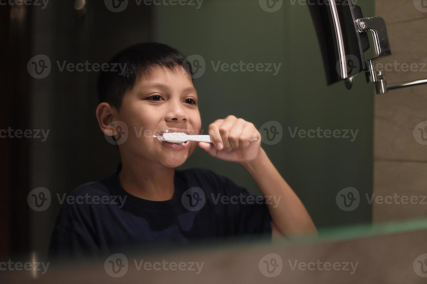 niño asiático cepillarse los dientes en el baño foto