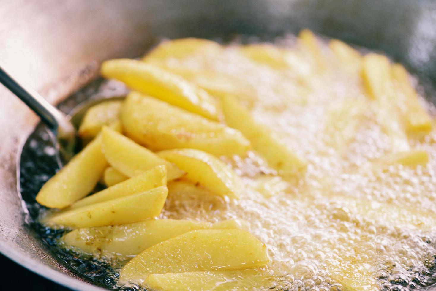 Cooking french fries or fry potatoes in hot oil for potato wedges, Close up fried potatoes in oil on pan photo