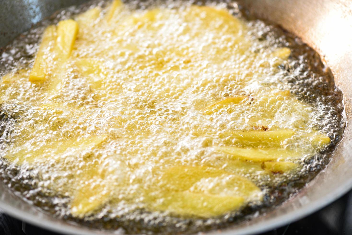 cocinar papas fritas o freír papas en aceite caliente para gajos de papa, cerrar papas fritas en aceite en una sartén foto